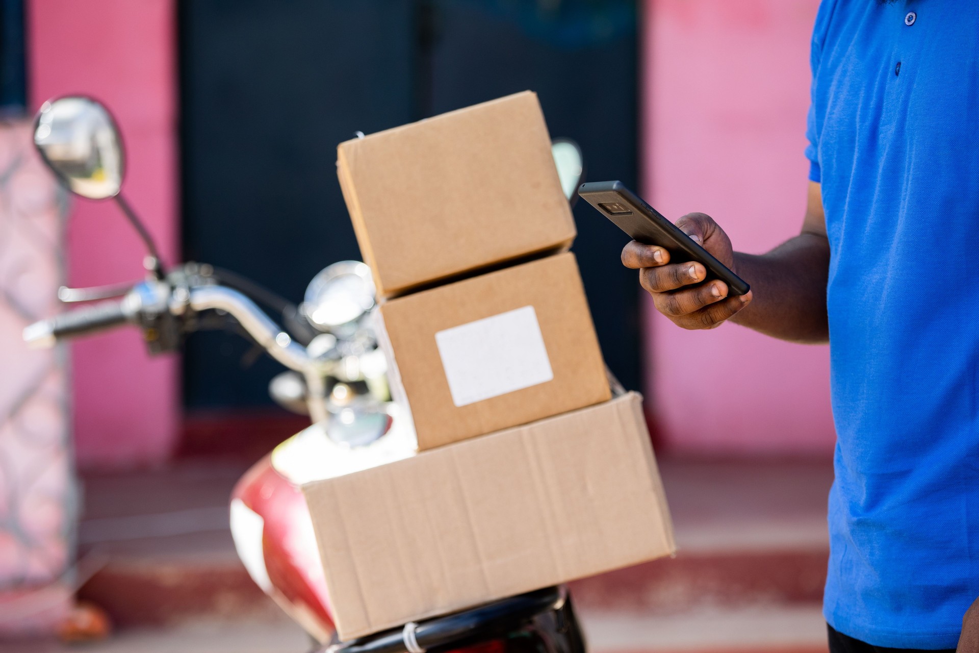 African Delivery Courier Man from Local Postal Shipping Service delivers Mail packages with motorcycle at Urban Home.